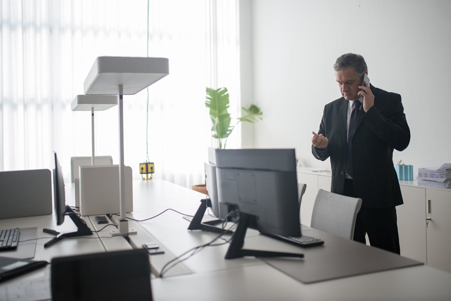 Man staande aan een bureau en met smartphone aan het bellen