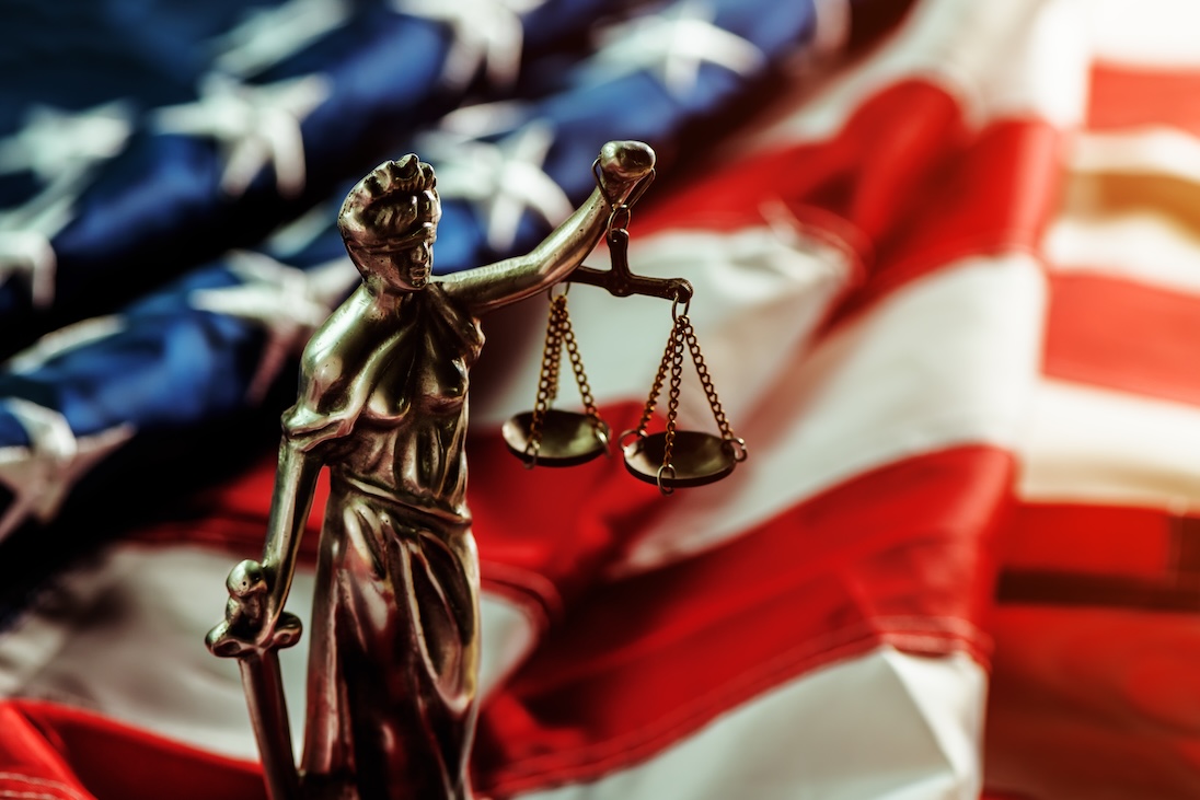Beeldje van Vrouwe justitia en op achtergrond de vlag van USA