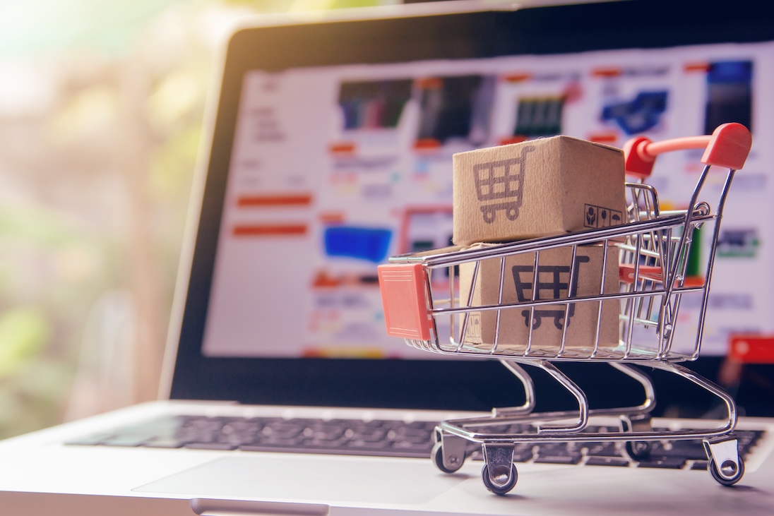 Laptop met op scherm een webwinkel en op toetsenbord een klein winkelwagentje met 2 doosjes