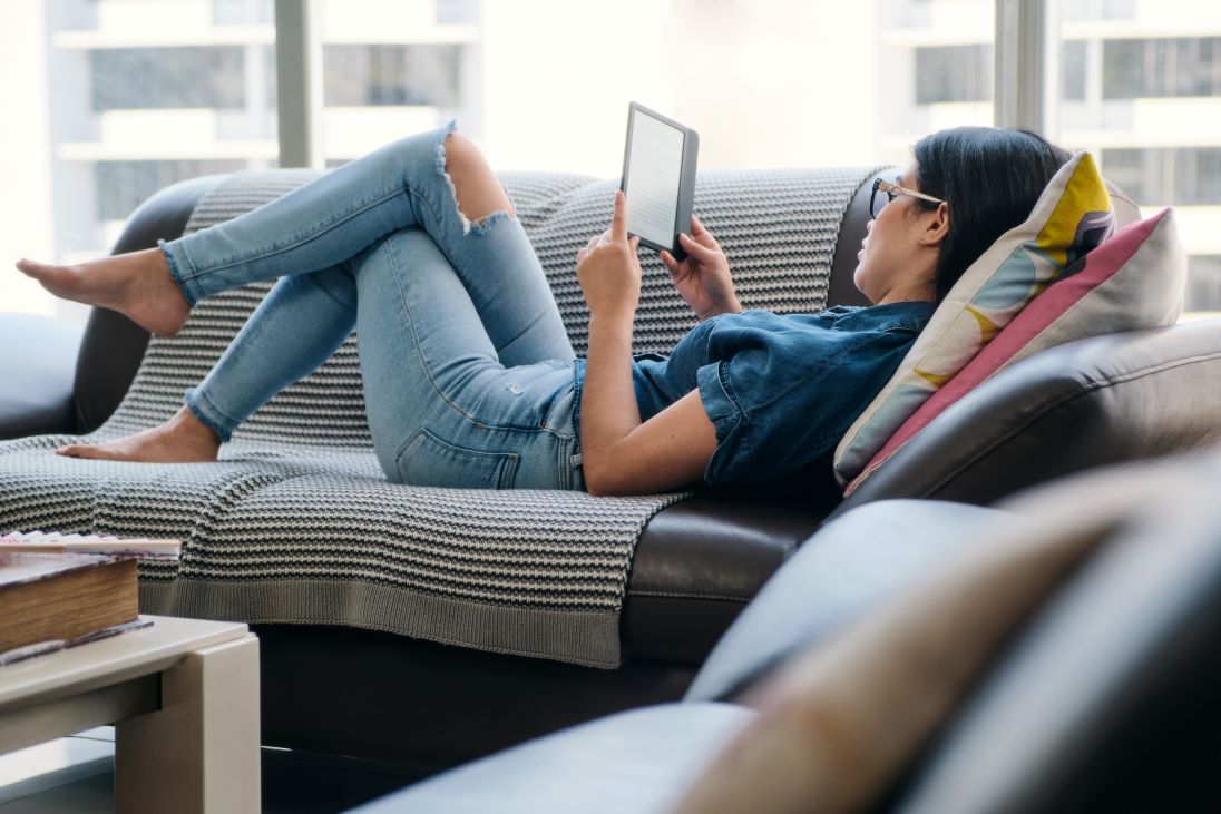 Vrouw leest languitliggend op sofa een ereader