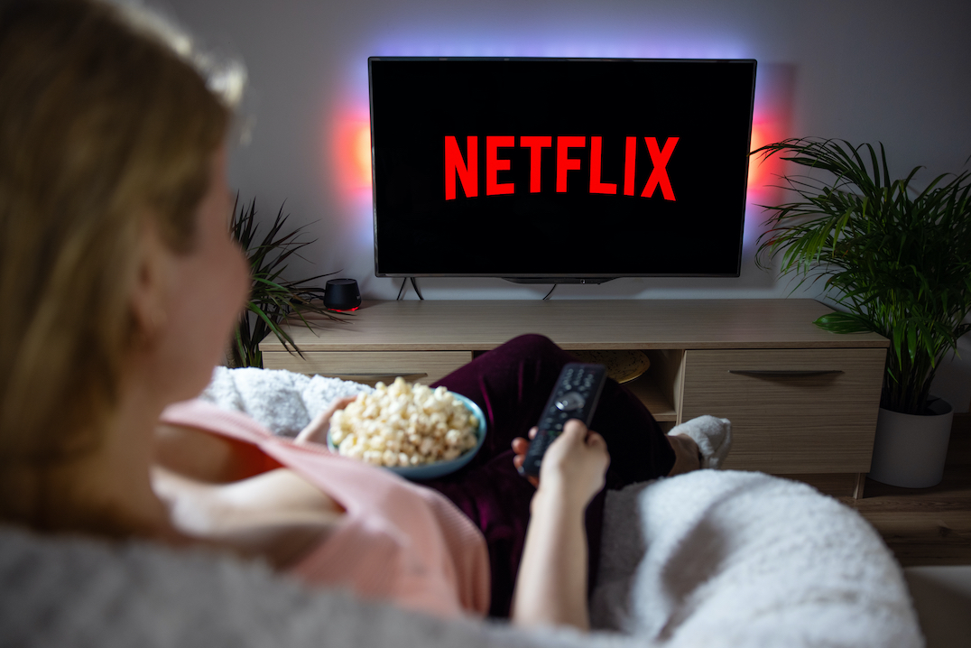 Vrouw kijkt naar Netflix met bak popcorn bij de hand en in andere hand de afstansdbediening