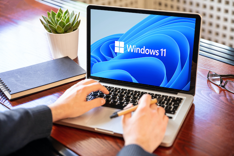 twee handen die met laptop toestenbord bezig zijn en op scherm logo Windows 11