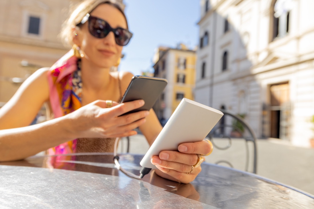 Vrouw op een terrasje die met een powerbank haar telefoon oplaadt
