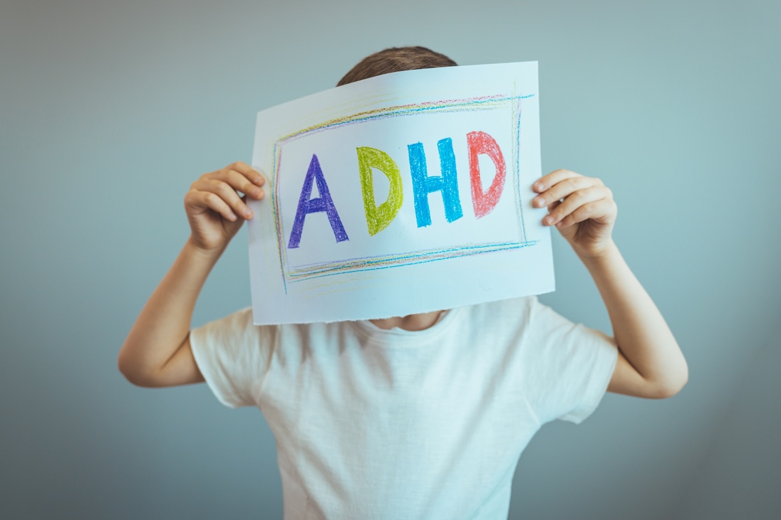 jong kind dat een boordje voor zijn of haar gezicht houdt met daarop groot geschreven ADHD