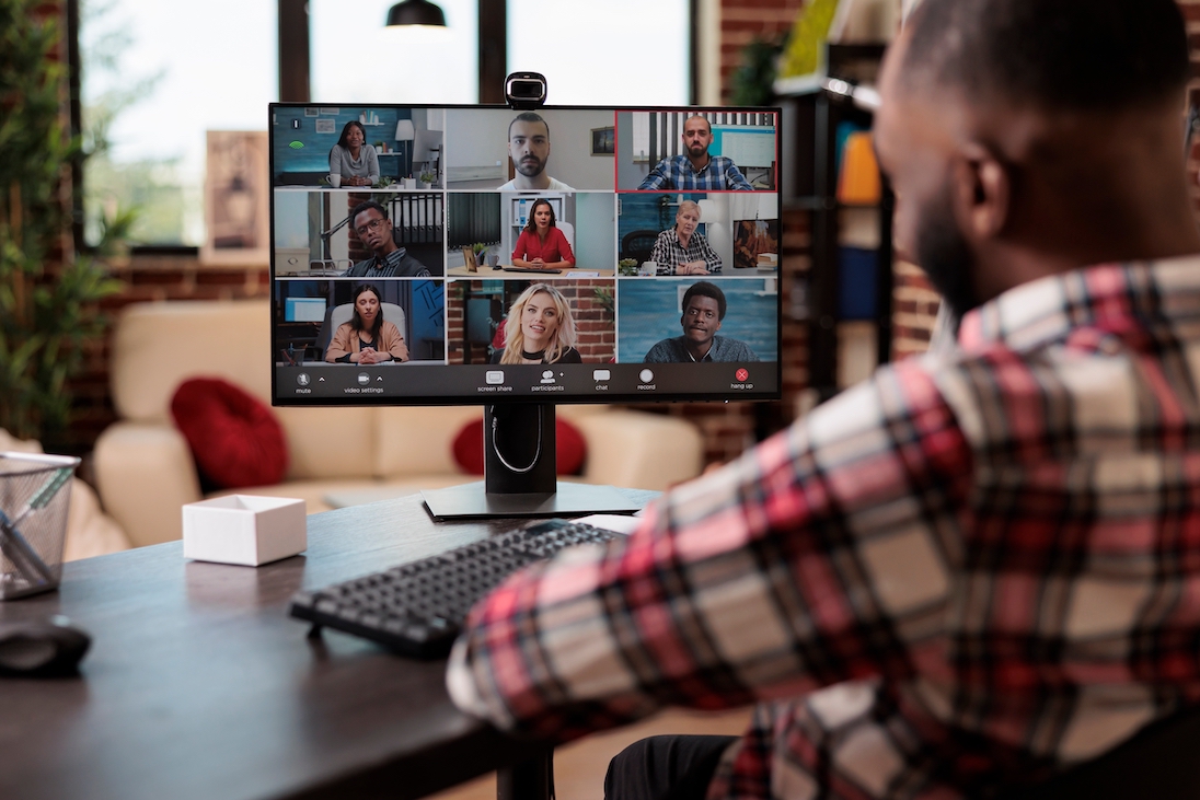 Man kijkt naar computerscherm mte daarop een videocall met meerdere deelnemers