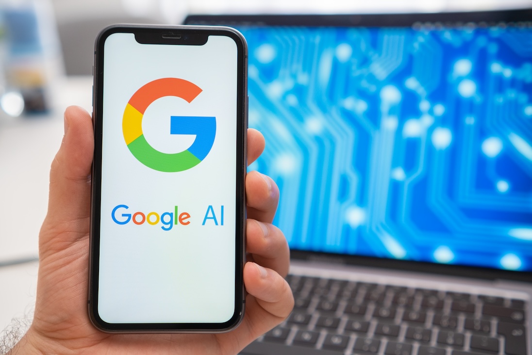 Google AI op smartphone op de achtergrond een opengeklapte laptop