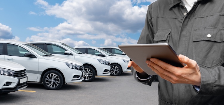 Man met tablet in zijn hand en op de achtergrond een rij witte auto's