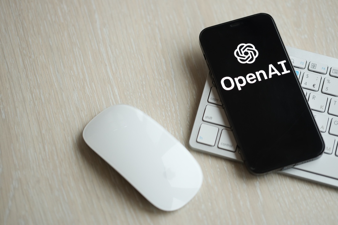 toetsenboord, muis en smartphone met daar op het scherm het logo van OPENAI
