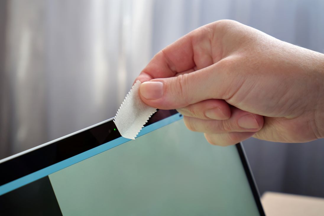 hand met een soort pleister die webcam van een laptop gaat afdekken