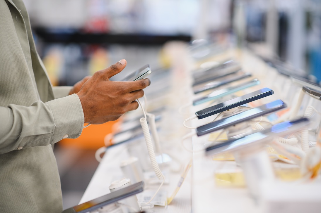 Klant die smartphone vasthoudt, nieuwe mobiele telefoon vergelijkt en kiest in elektronicawinkel