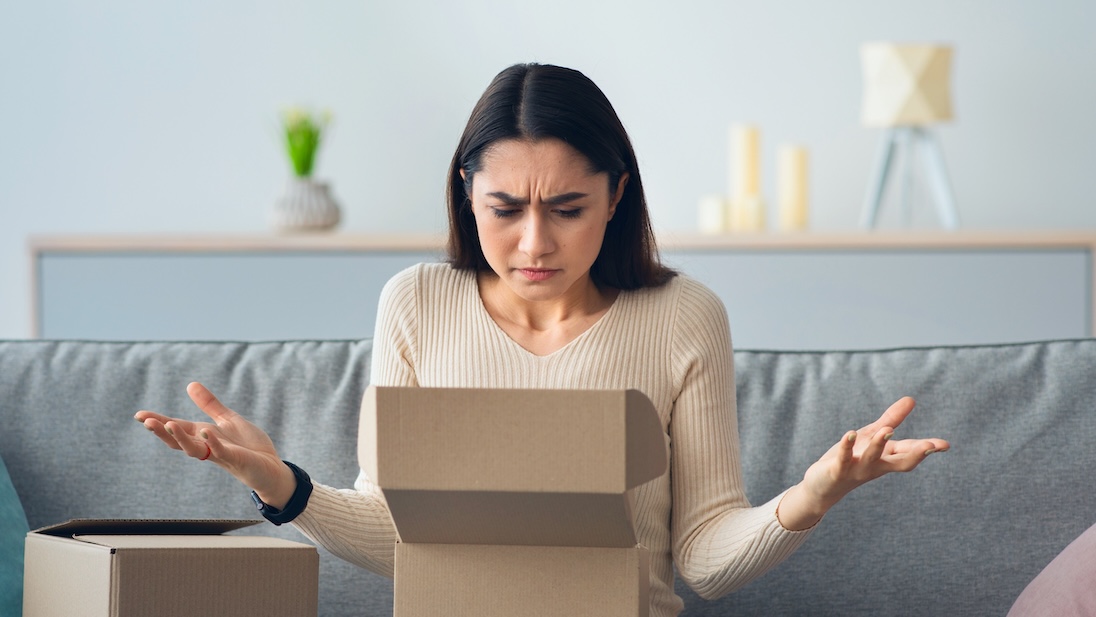 Jonge vrouw pakt een pakketje uit en kijkt teleurgesteld
