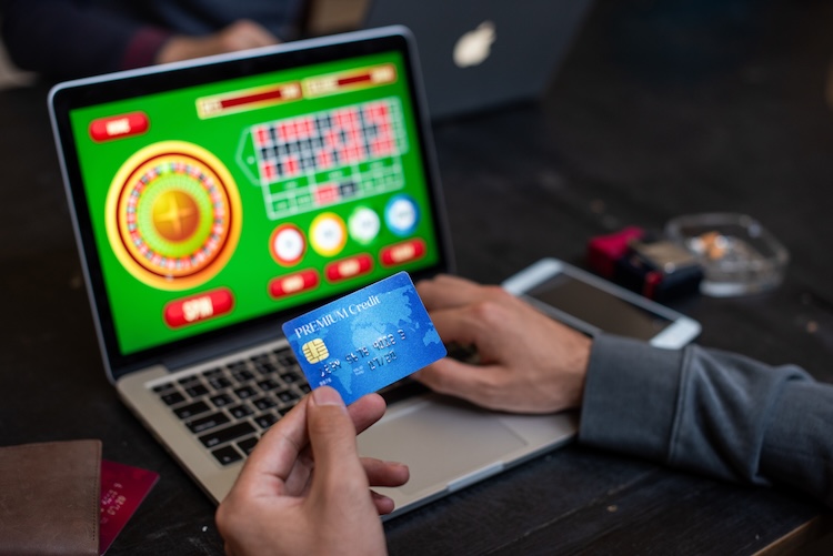 Man met creditcard in zijn hand en op zijn laptopscherm een online goksite