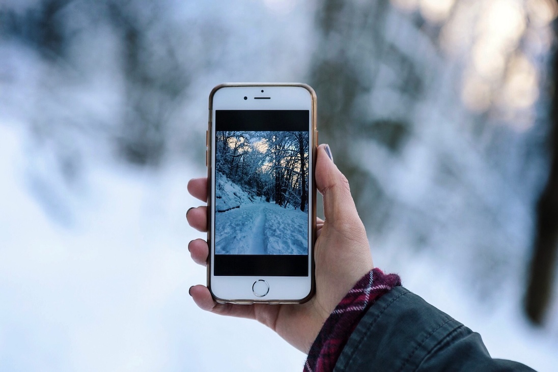 Hand die een iphone vasthoudt met op achtergrond een sneeuwlandschap